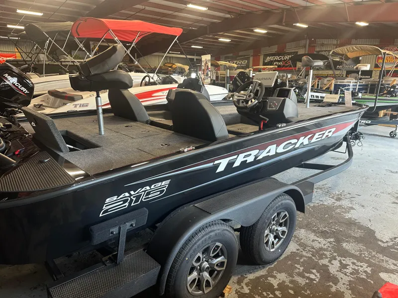 Slide: The Image of 2025 Tracker Savage 215 boat in showroom, black exterior, dual-axle trailer, indoor lighting. - 9