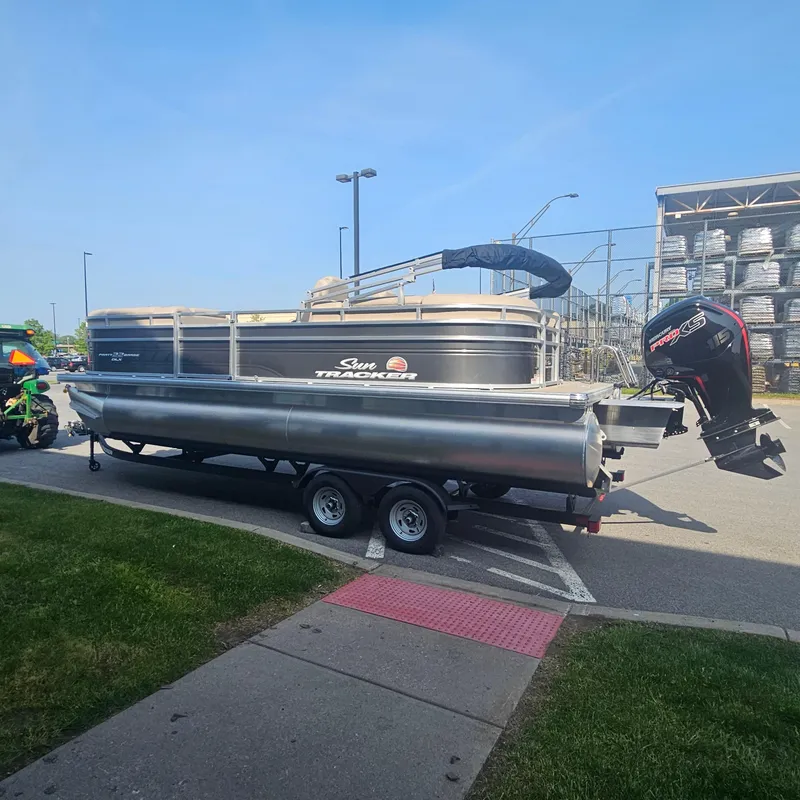 Slide: The Image of 2025 Sun Tracker Party Barge 22 DLX on trailer, parked outdoors. - 2