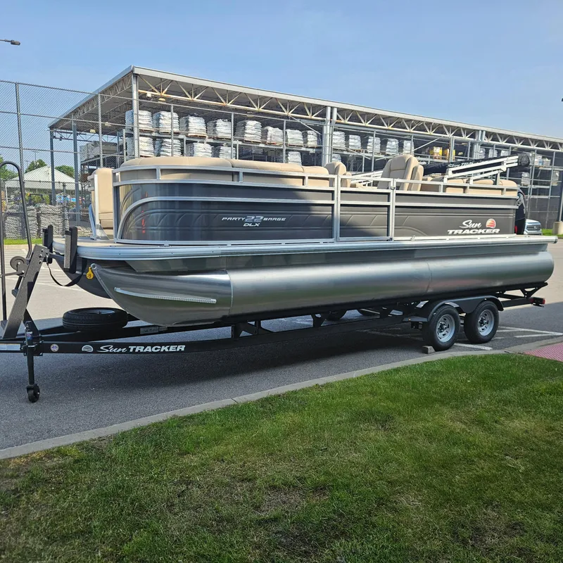 Slide: The Image of 2025 Sun Tracker Party Barge 22 DLX pontoon boat on trailer, parked outdoors. - 3