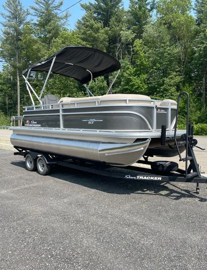 Slide: The Image of 2025 Sun Tracker Party Barge 20 DLX pontoon boat on trailer, parked outdoors. - 2