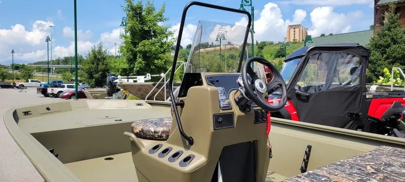 Slide: The Image of 2025 Tracker Grizzly 1860 CC boat with camouflage seats, parked outdoors on a sunny day. - 2