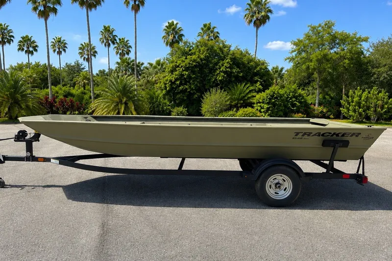 The Image of The image shows a Tracker Grizzly 1860 Utility boat on a trailer, surrounded by palm trees. - 0
