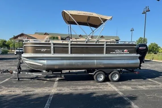 The Image of 2025 Sun Tracker SportFish 20 DLX pontoon boat on trailer in parking lot. - 0