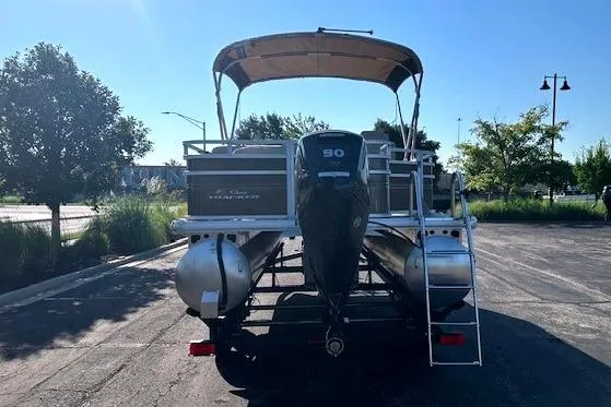 Slide: The Image of 2025 Sun Tracker SportFish 20 DLX pontoon boat with canopy and outboard motor in parking lot. - 2