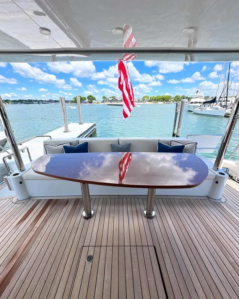 Slide: The Image of 2023 CL Yachts CLB65 aft deck with polished table, overlooking marina and blue skies. - 2