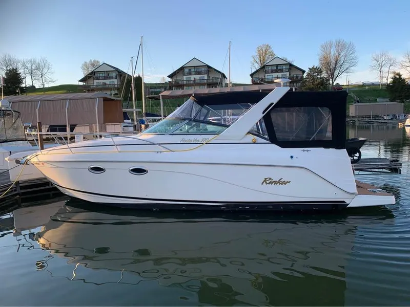 Slide: The Image of 2003 Rinker 270 boat docked in a marina, with scenic background. - 0