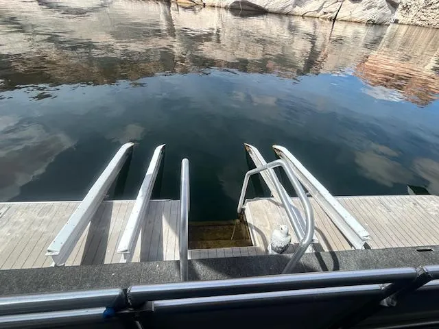 Slide: The Image of Adonia 2020 houseboat deck with water access ladder, reflecting calm waters and rocky shoreline. - 22