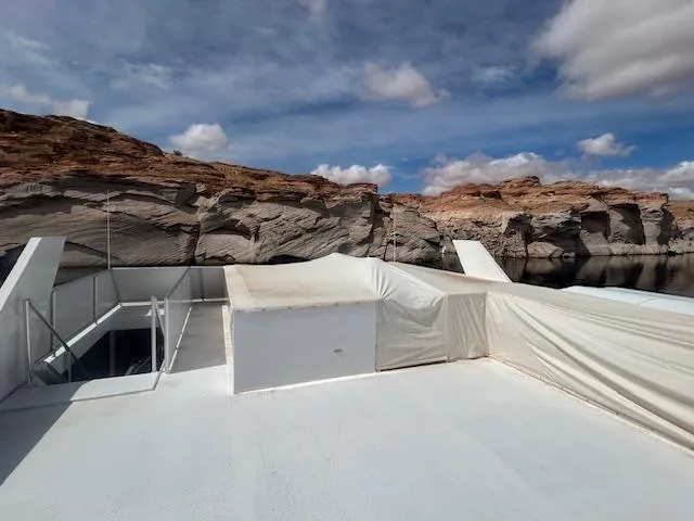 Slide: The Image of Adonia 2020 houseboat on calm water, rocky cliffs in the background, under a partly cloudy sky. - 34