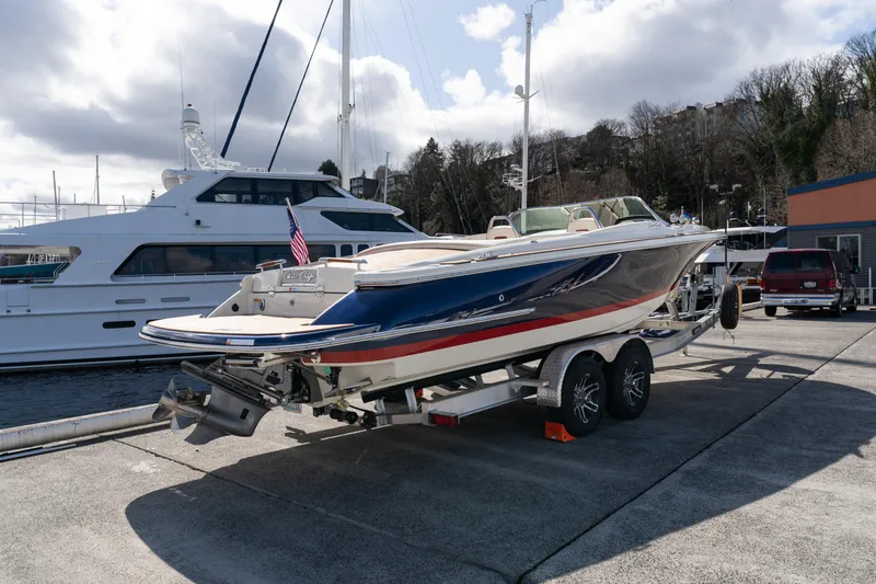 Slide: The Image of 2022 Chris-Craft Launch 27 boat on trailer, dockside with yachts in background. - 0