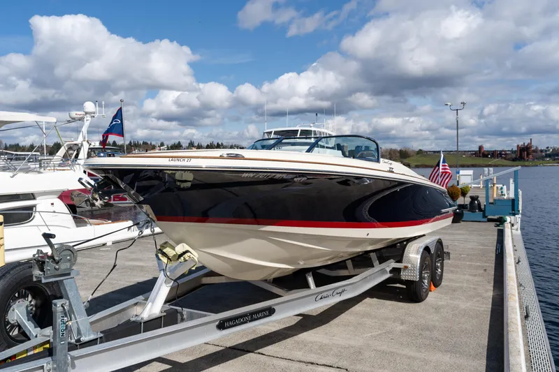 Slide: The Image of 2022 Chris-Craft Launch 27 boat on trailer at dockside, under cloudy sky. - 1