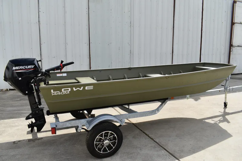 Slide: The Image of 2024 Lowe L1440M Jon boat with Mercury motor on trailer, parked outdoors. - 2