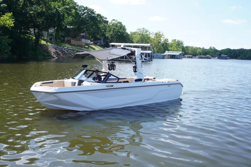 Slide: The Image of 2025 Nautique GS24 boat on a calm lake with trees in the background. - 2