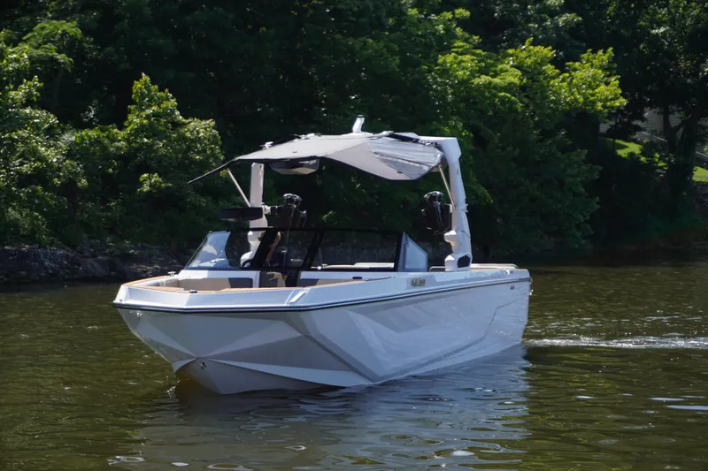 Slide: The Image of 2025 Nautique GS24 boat cruising on a calm lake with lush green trees. - 3