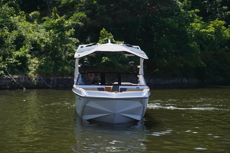 Slide: The Image of 2025 Nautique GS24 boat cruising on a calm lake surrounded by lush greenery. - 4