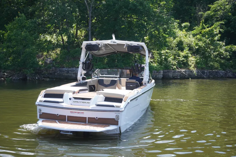 Slide: The Image of 2025 Nautique GS24 boat on a calm lake, surrounded by lush greenery. - 8