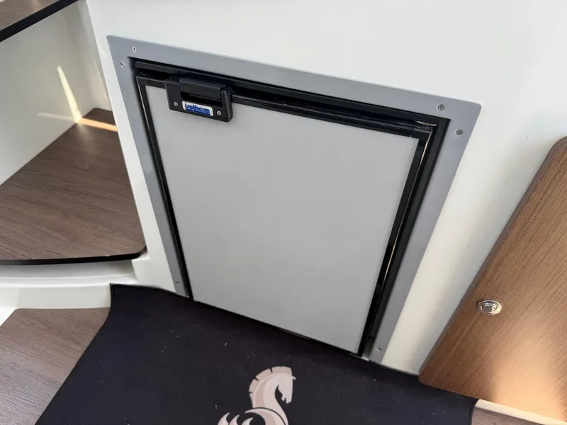 Slide: The Image of Compact fridge inside 2021 Beneteau Antares 8 boat cabin, featuring sleek design and wooden accents. - 21
