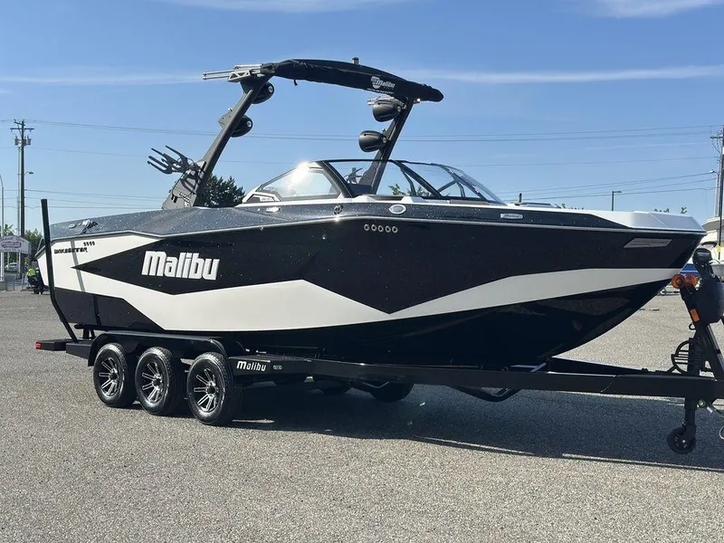 Slide: The Image of 2025 Malibu 25 LSV boat on trailer, sleek black and white design, parked outdoors. - 30