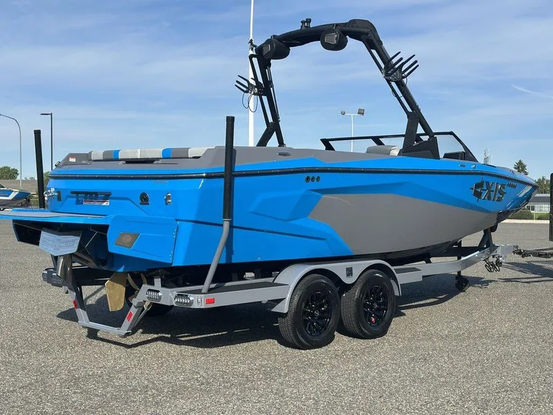 Slide: The Image of 2025 Axis A225 boat in vibrant blue and gray on a trailer, parked outdoors. - 25