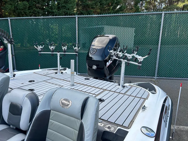 Slide: The Image of 2009 Triton 18 Explorer boat with fishing rod holders and motor, parked by a green fence. - 4