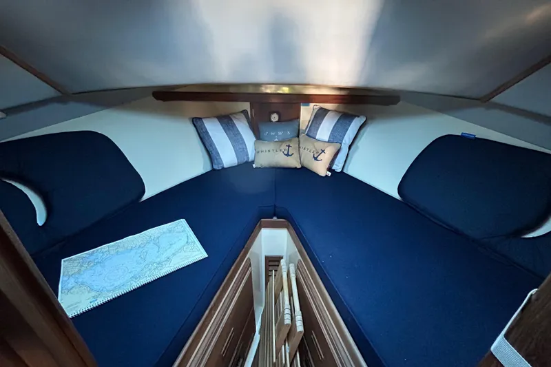 Slide: The Image of 1989 Fortier F-30 Hardtop cabin interior with blue cushions, nautical pillows, and a map. - 4