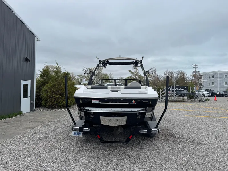 Slide: The Image of 2018 Malibu VLX boat parked on gravel near a building, rear view. - 7