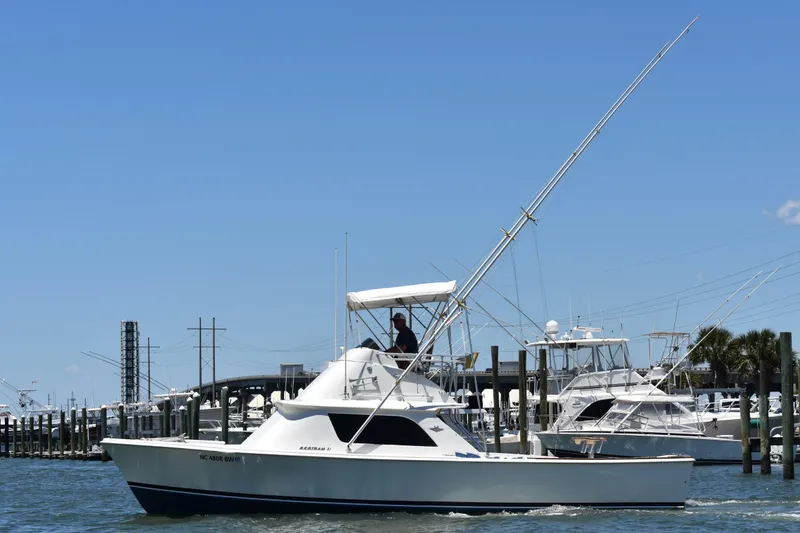 The Image of 1965 Bertram 31 boat cruising in a marina under a clear blue sky. - 1