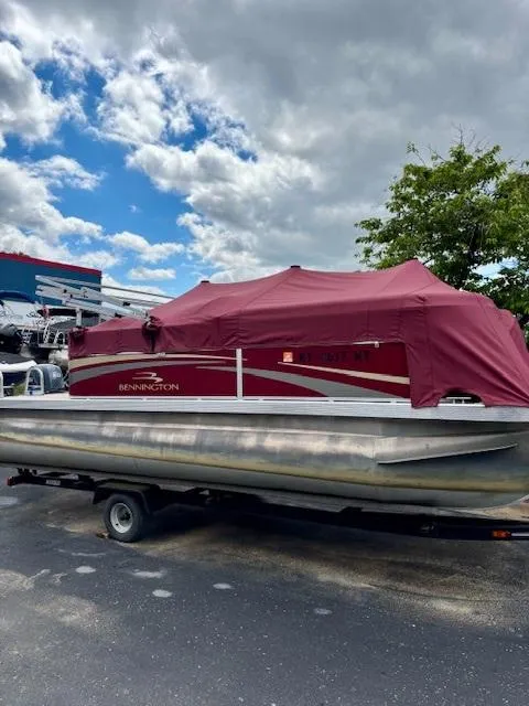 Slide: The Image of 2011 Bennington 20SLi pontoon boat with red cover on trailer, under cloudy sky. - 5