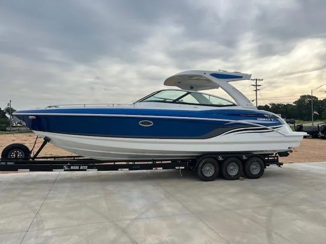 The Image of 2025 Formula 330 Crossover Bowrider I/O boat on trailer, blue and white design. - 1