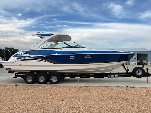Slide: The Image of 2025 Formula 330 Crossover Bowrider I/O on trailer, blue and white design, parked outdoors. - 5