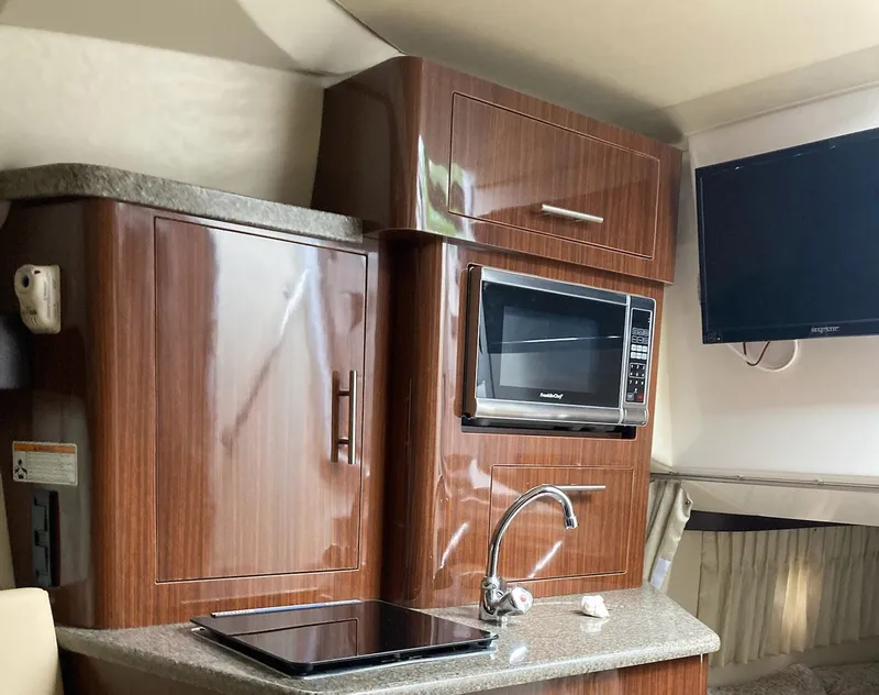 Slide: The Image of Interior of 2015 Regal 28 Express boat with kitchenette, featuring microwave, sink, and TV. - 7