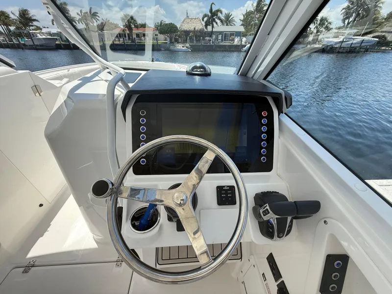 Slide: The Image of 2022 Edgewater 262 CX boat helm with steering wheel and control panel by the water. - 23