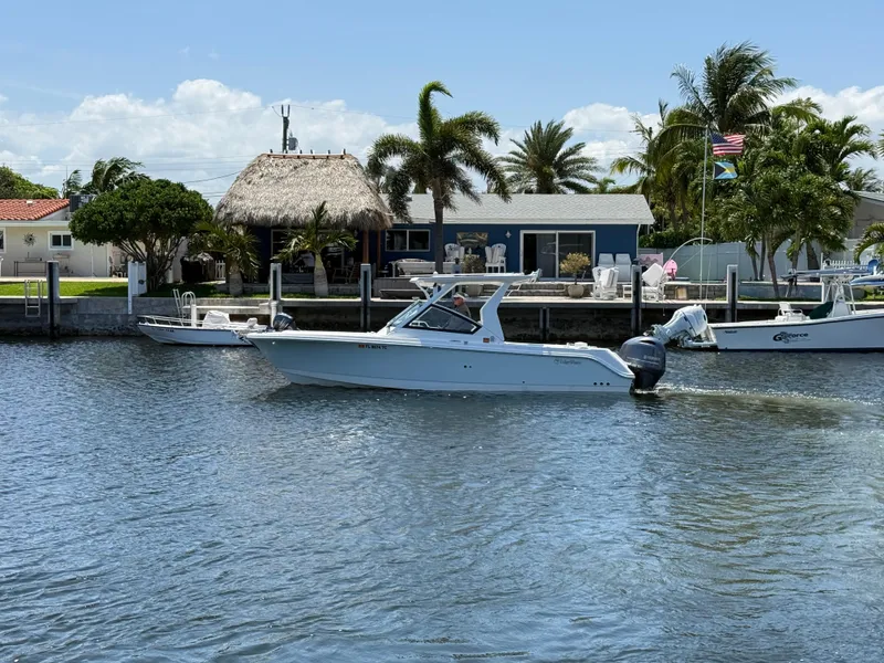 Slide: The Image of 2022 Edgewater 262 CX boat cruising on a sunny waterfront with palm trees and a thatched-roof house. - 7