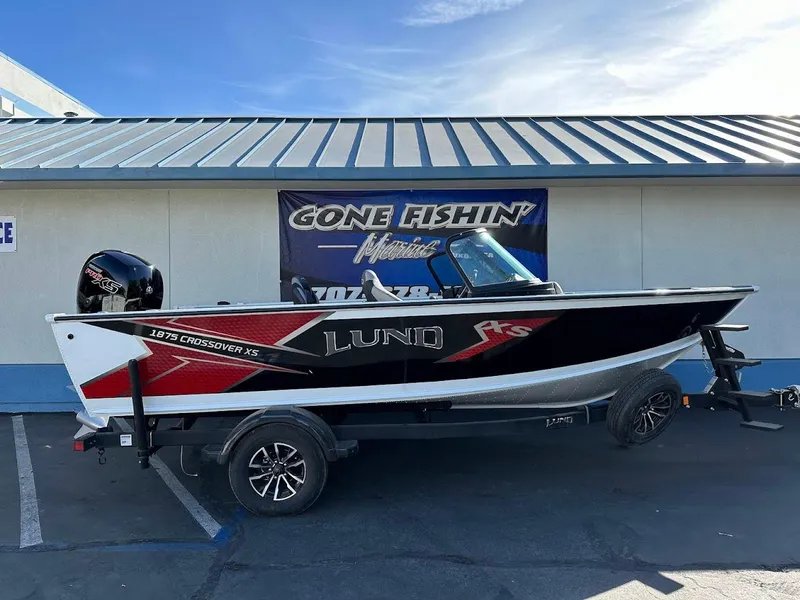 Slide: The Image of 2025 Lund 1875 Crossover XS boat on trailer, parked outside a building. - 0