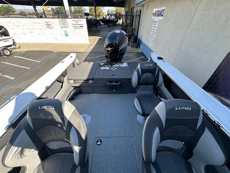 Slide: The Image of 2025 Lund 1875 Crossover XS boat interior with seating and motor, parked outdoors. - 13