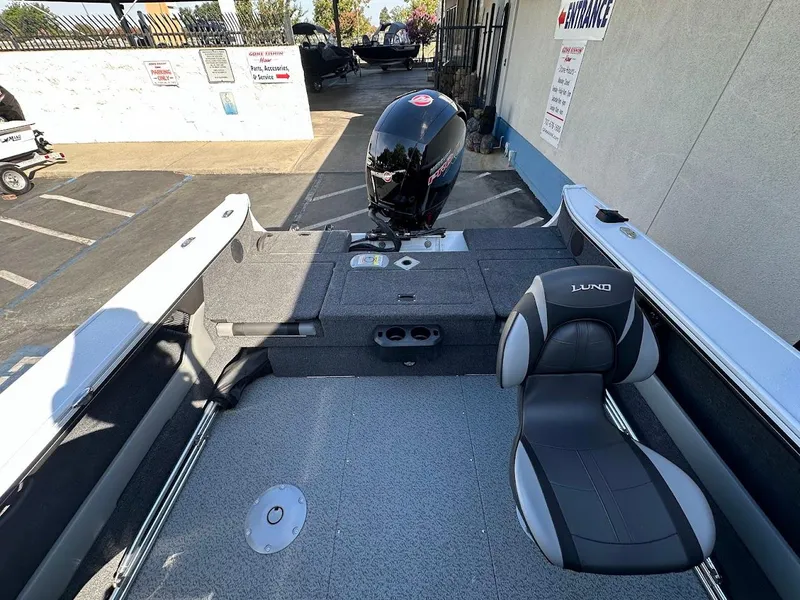 Slide: The Image of 2025 Lund 1875 Crossover XS boat interior with seating and motor, parked outdoors. - 14