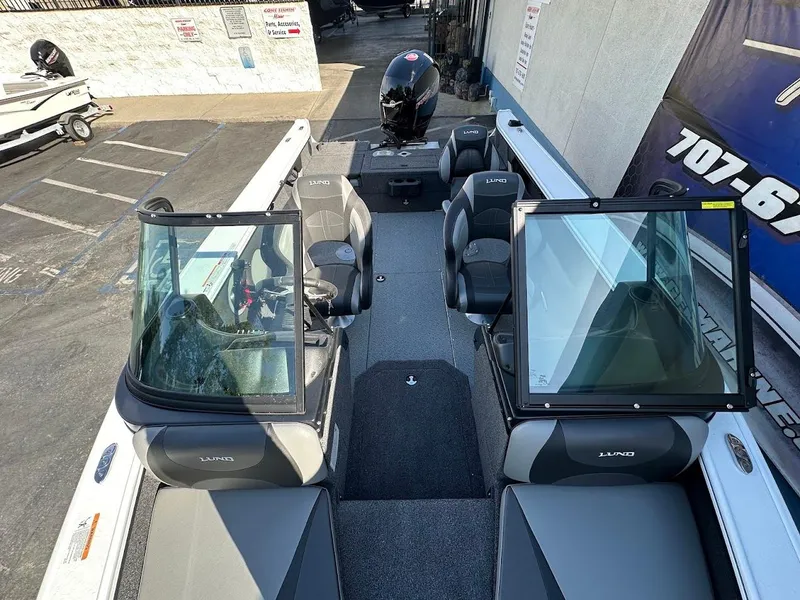 Slide: The Image of 2025 Lund 1875 Crossover XS boat interior with seating and windshield, parked outdoors. - 27