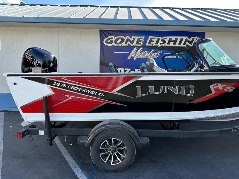 Slide: The Image of 2025 Lund 1875 Crossover XS boat on trailer, displayed at a marine dealership. - 6