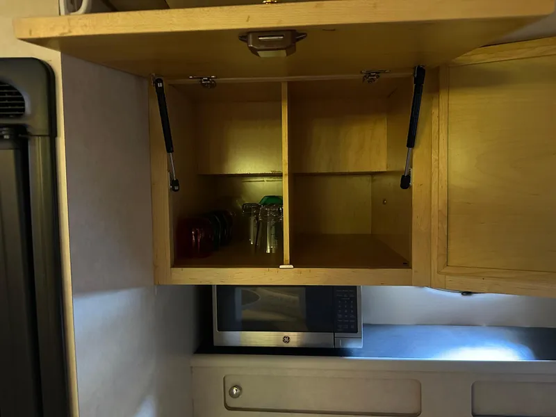 Slide: The Image of Open wooden cabinet in 1997 Regal Commodore 402 kitchen, with glasses and a microwave below. - 37