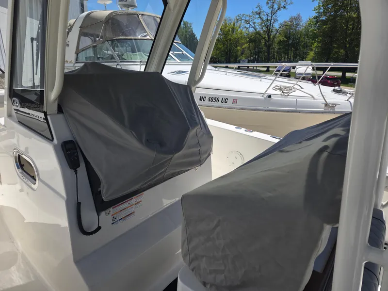 Slide: The Image of 2025 Pursuit S 288 Sport boat interior with covered controls, docked near other boats. - 34