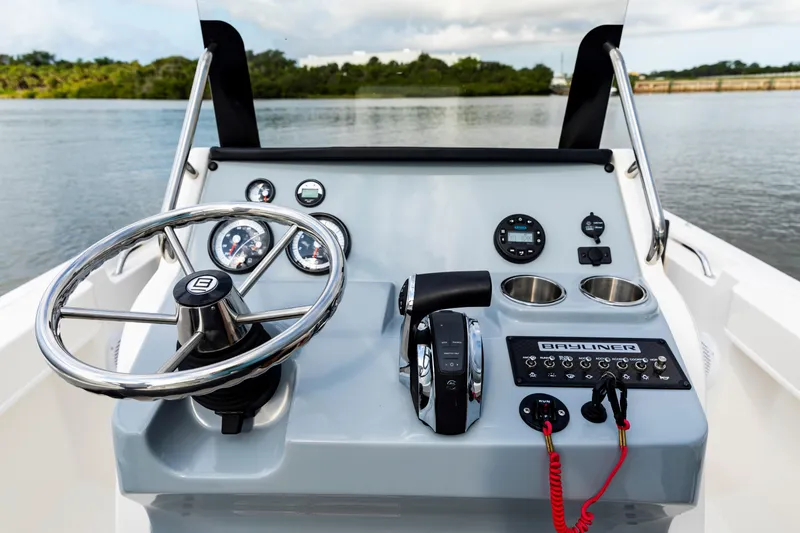 Slide: The Image of 2023 Bayliner Trophy 20CC boat dashboard with steering wheel and controls on a calm water backdrop. - 25