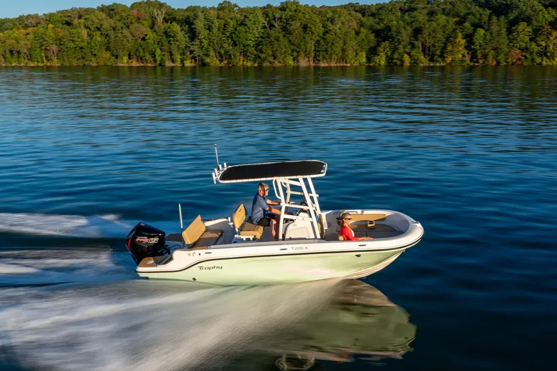 Slide: The Image of 2024 Bayliner Trophy 20CX boat cruising on a serene lake with lush green forest backdrop. - 5