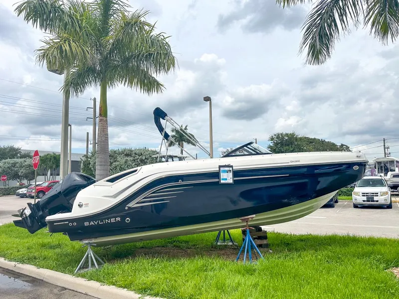 Slide: The Image of 2024 Bayliner DX2200 boat displayed outdoors on stands, surrounded by palm trees. - 2