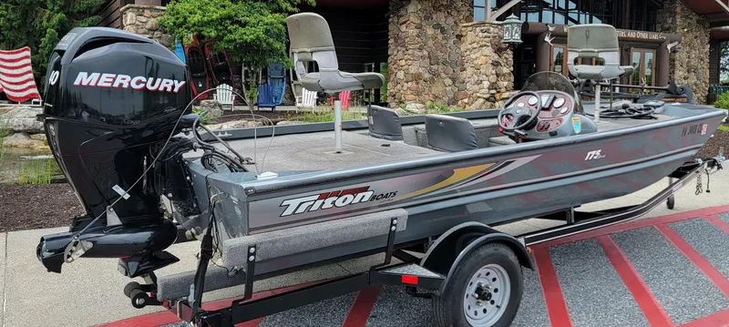 Slide: The Image of 2002 Triton 175 Sport boat with Mercury engine on trailer, parked near stone building. - 0