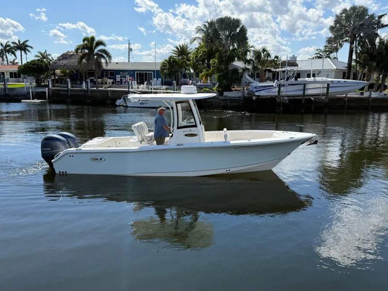 Slide: The Image of 2023 Sea Hunt Gamefish 25 boat on calm water, surrounded by palm trees and docks. - 7