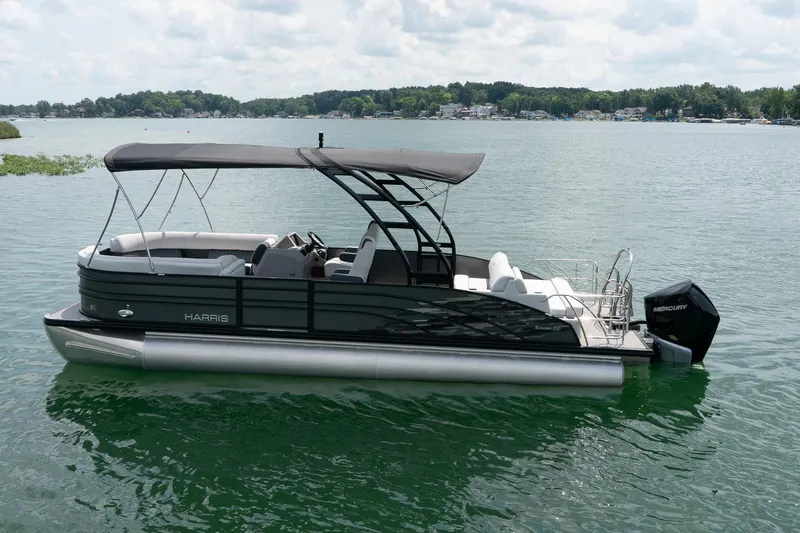Slide: The Image of 2023 Harris 250 Sunliner Sport pontoon boat on a lake with canopy and outboard motor. - 1