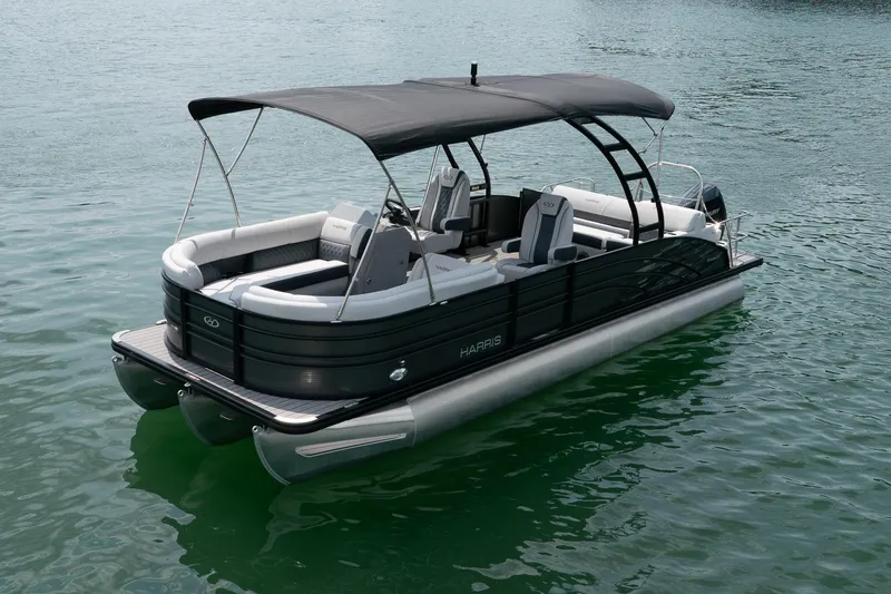 Slide: The Image of 2023 Harris 250 Sunliner Sport pontoon boat on calm water, featuring sleek design and canopy. - 2