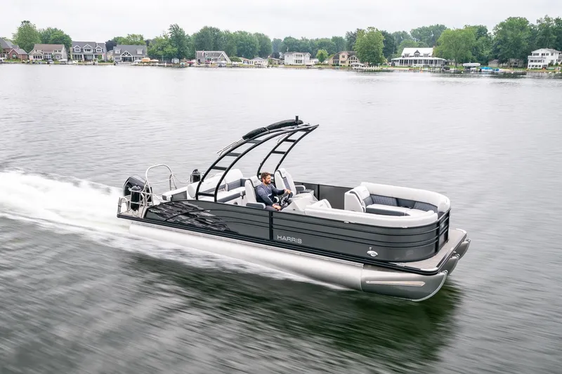 Slide: The Image of 2023 Harris 250 Sunliner Sport pontoon boat cruising on a lake with scenic background. - 4