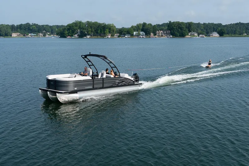Slide: The Image of 2023 Harris 250 Sunliner Sport pontoon boat towing a water skier on a scenic lake. - 6