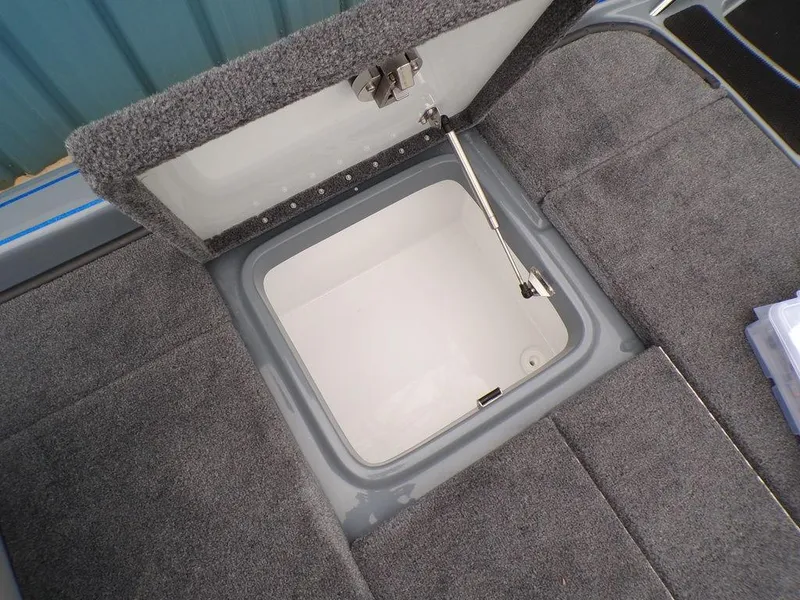 Slide: The Image of Open storage compartment in 2025 Phoenix 921 ELITE boat, featuring gray carpeted interior. - 2