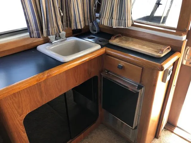 Slide: The Image of 1988 Bayliner 3818 Motoryacht kitchen with sink, countertop, and striped curtains. - 16